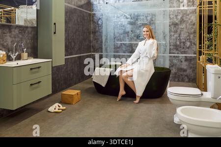 Lächelnde positive europäische Frau posiert auf der Badewanne im Bad, geht baden Stockfoto