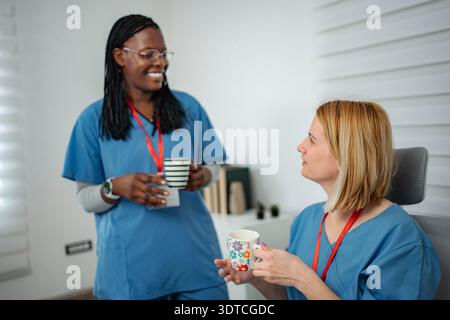 Verschiedene Krankenschwestern machen Kaffeepause, reden und lächeln Stockfoto