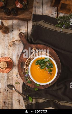 Ein lebhaftes orangenes Gemüsepüree, serviert in einer weißen Schüssel auf einem rustikalen Holzbrett. Die flache Komposition bietet warmes natürliches Licht und erdigen Text Stockfoto