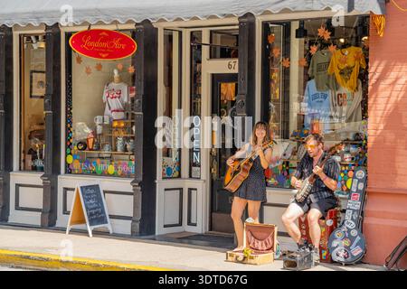 Arkansas, 21. SEP 2024: Zwei Straßenkünstler schlagen Akustikgitarren vor einer bunten Boutique mit londoner Flugzeugschild. Stockfoto