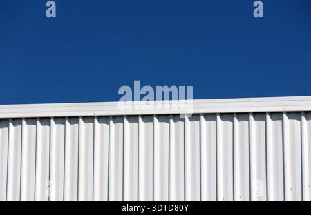 Oberer Teil eines Gebäudes aus weißem Wellblech vor blauem Himmel Stockfoto