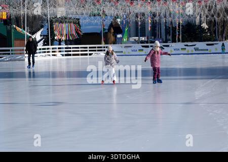 Zwei Kinder laufen in der Wintersonne spielerisch auf einer glitzernden Eisbahn. Kiew, Ukraine. Februar 2026. National Complex Expocenter der Ukraine, Ma Stockfoto