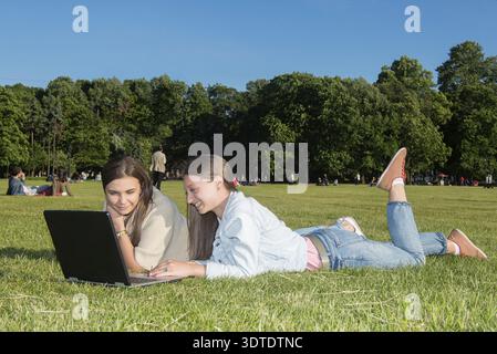 Zwei Freunde mit Tablet-Computer sitzen auf dem Gras im Sommerpark. Jugendstil Stockfoto