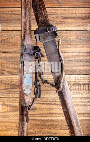 Antike Holzskier mit Lederbindungen vor rustikalem Holzhintergrund Stockfoto