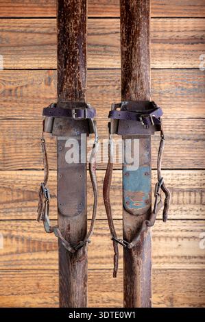 Antike Holzskier mit Lederbindungen vor rustikalem Holzhintergrund Stockfoto