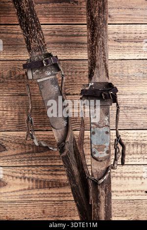 Antike Holzskier mit Lederbindungen vor rustikalem Holzhintergrund Stockfoto