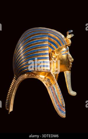 Goldene Grabmaske von Tutanchamun im Seitenprofil mit blauen und goldenen Streifen isoliert auf dunklem Hintergrund. Detaillierte alte ägyptische Pharaonenkörner Stockfoto