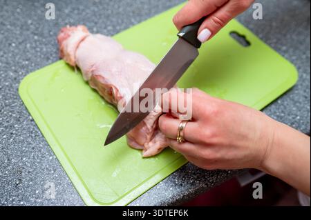 Nahaufnahme einer Person, die frisches rohes Geflügelfleisch auf einem grünen Schneidebrett schneidet. Konzept der Hausmannskost, Lebensmittelzubereitung, gesunde Ernährung und Vorbereitung Stockfoto