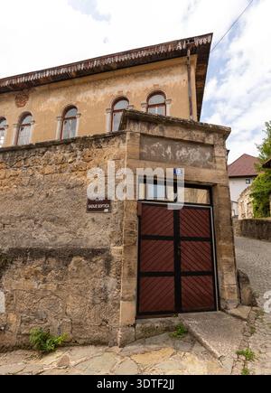 Historisches Gebäude mit verwitterter Steinmauer, Holztor und Bogenfenstern entlang der Ulica Sadue Softica in Jajce, Bosnien und Herzegowina. Stockfoto
