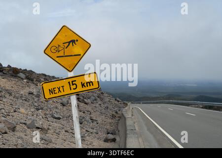 Radfahrer kümmern sich um das nächste 15 km Warnschild. Gelbes und schwarzes diamantförmiges Schild mit einem Symbol, das einen Radfahrer zeigt, der über die Vorderseite seines Fahrrads fällt. Stockfoto