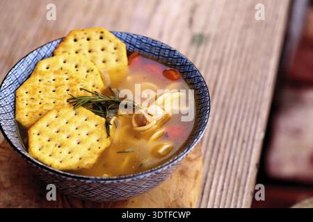 Hühnernudelsuppe in einer blau-weißen Schüssel mit Crackern, alle auf einem Holzschneidebrett Stockfoto