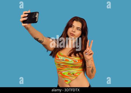 Junge Frau, die ein Selfie macht, mit einem Smartphone auf blauem Hintergrund Stockfoto