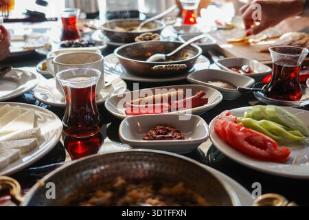 Reichhaltiges traditionelles türkisches Frühstück mit Käse, Oliven, Würstchen, Tomaten, Gurken, Gebäck, Marmelade und schwarzer Tee in Tulpengläsern, Hands se Stockfoto