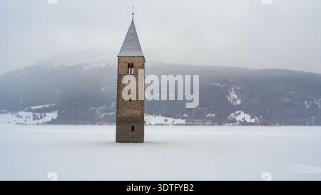 Mittelalterlicher untergetauchter Glockenturm im Reschensee im Winter. Ein beeindruckender Winterblick auf den untergetauchten Kirchturm des Kurer Vinschgaus aus dem 14. Jahrhundert. Stockfoto
