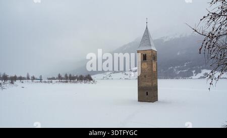Mittelalterlicher untergetauchter Glockenturm im Reschensee im Winter. Ein beeindruckender Winterblick auf den untergetauchten Kirchturm des Kurer Vinschgaus aus dem 14. Jahrhundert. Stockfoto