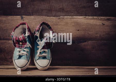 Ein Paar Sneakers mit farbenfrohem kariertem Stoff auf Zunge und Ferse, weißen Schnürsenkeln und weißen Zehen, die auf einem Holzboden an einer Holzwand platziert sind. Stockfoto