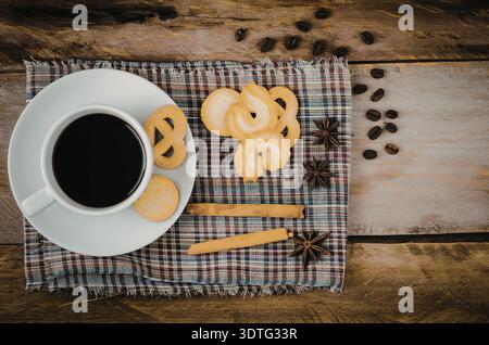 Eine warme und einladende Szene mit einer Tasse Kaffee, Donuts und Gewürzen auf einem rustikalen Holztisch. Stockfoto