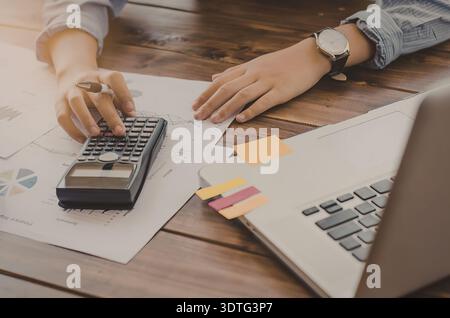 Eine Person arbeitet mit einem Taschenrechner und einem Laptop an Finanzdokumenten. Stockfoto