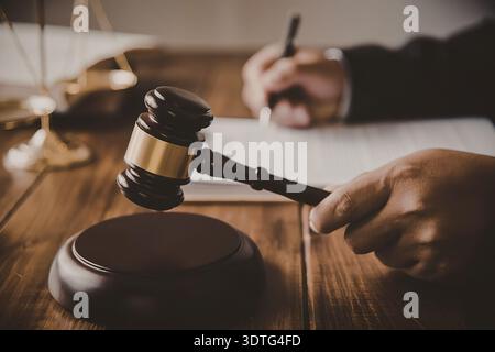 Eine Nahaufnahme des Hambers eines Richters, der auf einem hölzernen Schreibtisch liegt, mit einem verschwommenen Hintergrund einer Person, die auf Papiere schreibt. Stockfoto