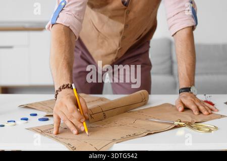 Männlicher Schneider, der mit Muster am Tisch im Atelier arbeitet, Nahaufnahme Stockfoto