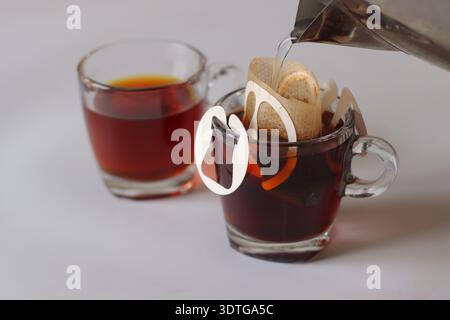 Filterbeutel für eine Tasse Tropfkaffee, der auf einer Glasschale liegt, während heißes Wasser für die manuelle Zubereitung gegossen wird. Frischer schwarzer Kaffee, zubereitet mit einem hängenden Papi Stockfoto