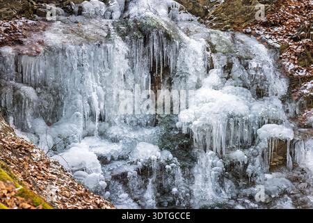 Ein gefrorener Wasserfall, der sich durch das felsige Gelände stürzt, mit filigranen Eiszapfen, die sich im Winter bilden und eine atemberaubende Darstellung des Künstlers der Natur schaffen Stockfoto