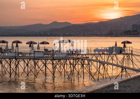 Beach Pier mit Sonnenschirmen bei Sonnenuntergang an der französischen Riviera von Cannes Stockfoto