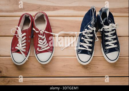 Ein Paar rote und blaue Converse-Schuhe, die mit einer herzförmigen Spitze auf einem hölzernen Hintergrund verbunden sind Stockfoto