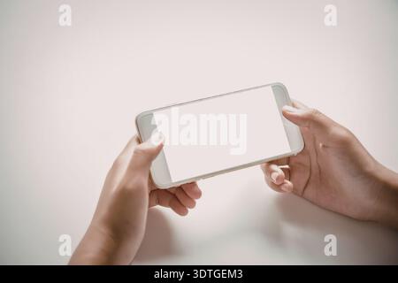 Ein Paar Hände, die ein weißes Smartphone mit einem leeren Bildschirm auf weißem Hintergrund halten. Stockfoto