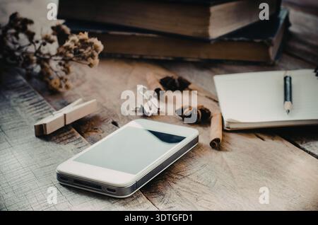 Ein Smartphone, Bücher, ein Notebook, Stift und verschiedene Gegenstände auf einer Holzoberfläche Stockfoto