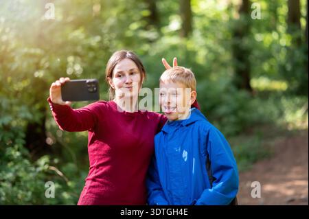 Mutter und Sohn machen lustige Gesichter, während sie ein Selfie während eines Frühlingswaldspaziergangs machen und die spielerische Familienzeit in der Natur genießen Stockfoto