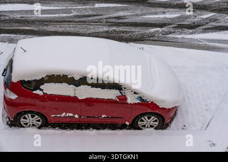 Schneebedecktes rotes Auto. Purpurroter Hatchback versteckt unter frischem Winterschnee. Scharlachrote Kompaktwagen, bedeckt mit eisweißem Pulver auf der Seitenstraße Stockfoto