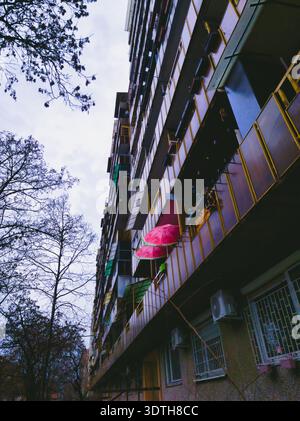 Ein beeindruckender vertikaler Blick auf ein Hochhaus mit farbenfrohen pinkfarbenen Regenschirmen. Dieses Bild zeigt den Schnittpunkt von privatem Haus Stockfoto