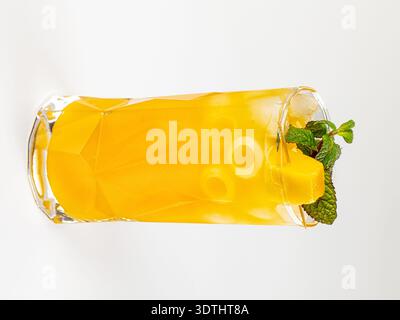Ein lebhafter gelber Mangococktail in einem hohen, facettierten Glas, gefüllt mit Eiswürfeln, garniert mit frischer Minze. Helle, hochwertige Beleuchtung auf einem sauberen weiß Stockfoto