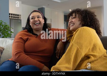 Verschiedene Freundinnen lachen und sitzen zu Hause auf der Couch, tragen Rost- und Senfpullover Stockfoto