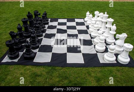 Übergroßes Western Schach-Set im Freien auf einer großen schwarz-weißen karierten Matte auf dem Gras Stockfoto