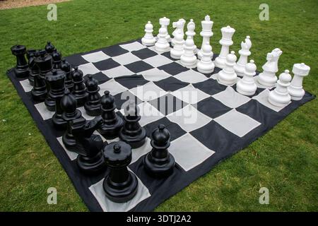 Übergroßes Western Schach-Set im Freien auf einer großen schwarz-weißen karierten Matte auf dem Gras Stockfoto