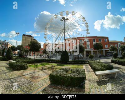 Latina, Italien - Februar 2026: Riesiges Riesenrad auf der Piazza del Popolo an einem sonnigen Wintertag, umgeben von rationalistischer Architektur und Stadtgärten Stockfoto
