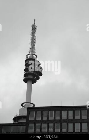 Schwarz-weiß-Blick auf einen Kommunikationsturm über Backsteinbürogebäuden in Amsterdam, Niederlande, unter einer dramatischen, bewölkten Winterskyline. Stockfoto