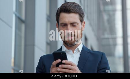 Erwachsener kaukasischer Geschäftsmann hält Smartphone Handy in der Stadt Geschäftsmann mit moderner Technologie-App außerhalb des Büros männlicher Arbeitgeber mittleren Alters Stockfoto