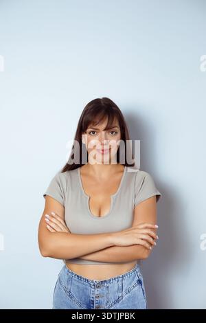 Ernste Frau, die mit gekreuzten Armen auf hellem Hintergrund steht. Stockfoto