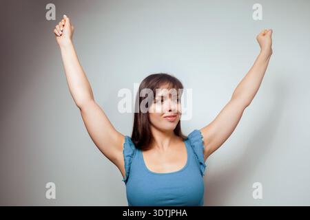Selbstbewusste junge Frau, die im Sieg die Arme hebt, isoliert auf Studiohintergrund. Stockfoto