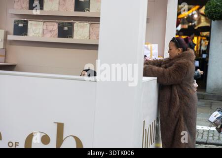 London, Großbritannien, 12. Dezember 2025, Frau in einem Kunstpelzmantel, die sich die Ausstellung eines Pop-up-Shops des House of CB ansieht. Covent Garden Stockfoto