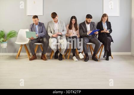 Gruppe von Bewerbern, die in Reihe sitzen und Formulare ausfüllen, während sie auf das Vorstellungsgespräch im Amt warten. Stockfoto