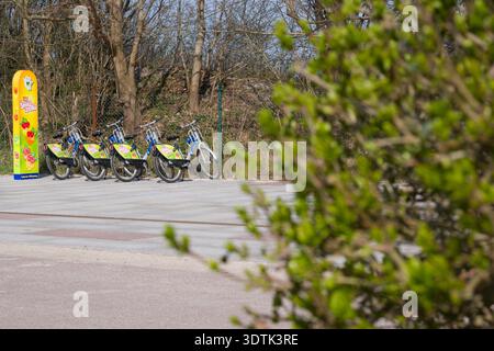 Eine Reihe von Fahrrädern, die an einer farbenfrohen Fahrradstation geparkt werden können. Die Szene findet an einem sonnigen Frühlingstag im Freien statt, neben einem Pfad in einem Park oder Stockfoto