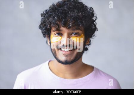 Junger Mann mit lockigen Haaren lächelt, während er Gesichtspflege für Hautpflege trägt Stockfoto