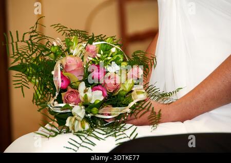 Eine Nahaufnahme zeigt einen eleganten Brautstrauß mit weichen rosa Rosen, leuchtendem magentafarbenen Ranunkeln, weißen Blumen und üppigem grünen Farnlaub. Stockfoto
