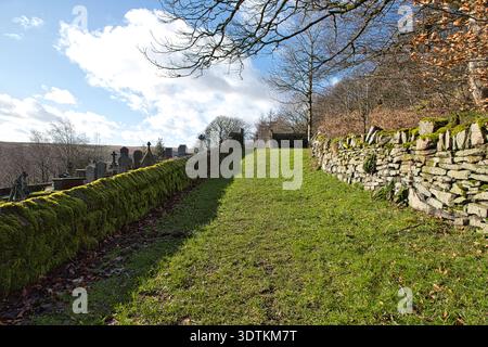 Grasbewachsener Pfad, gesäumt von moosbedeckten Trockenmauern, der vom Kirchhof St. Bartholomew in Richtung eines geschlossenen Ausgangs bei Scammonden, West Yorkshire, führt. Stockfoto