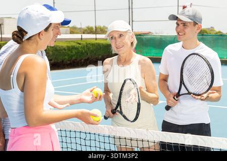 Eine Gruppe von Tennisspielern steht an warmen Tagen auf dem offenen Platz mit Schlägern und Bällen in den Händen, freundliche Gespräche nach dem Spiel Stockfoto