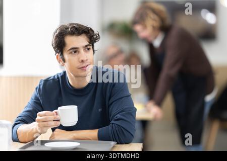 Hübscher junger Kerl, der frischen Kaffee am Tisch im Café trinkt Stockfoto